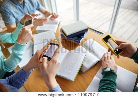 people, education, technology and exam concept - close up of students with smartphones taking picture of books page and making cheat sheet in school library