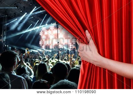 Human hand opens red curtain on concert scene background