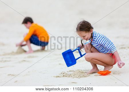 Two kids making sand castle and playing at tropical beach