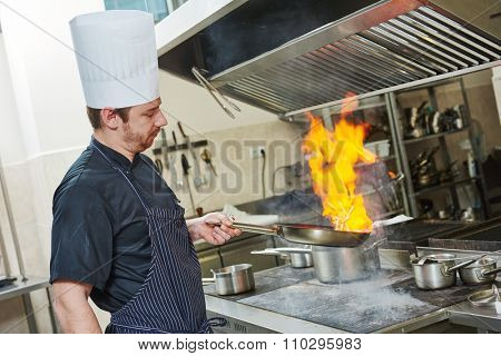 Food preparation. Chef cook in restaurant kitchen with pan over stove doing flambe 