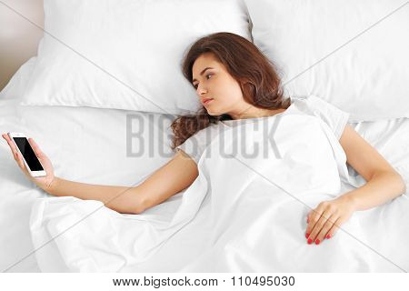 Beautiful young woman waking up with mobile alarm clock