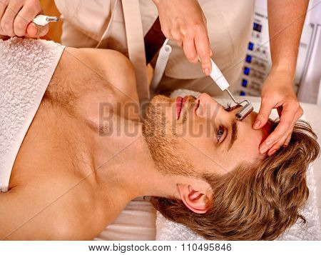 Young man looking up receiving electric galvanic face spa massage at beauty salon. 