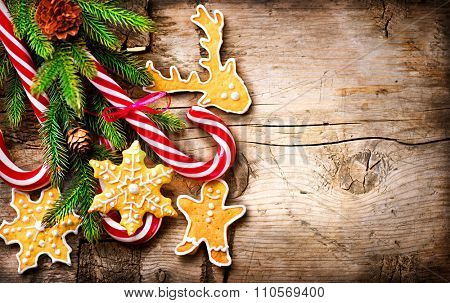 Christmas Holiday Background with Gingerbread cookies, Candy Cane and evergreens border over wooden table. Christmas and New year food. Christmas decoration and sweets on wood background