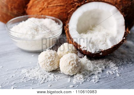 Candies in coconut flakes and fresh coconut on color wooden background