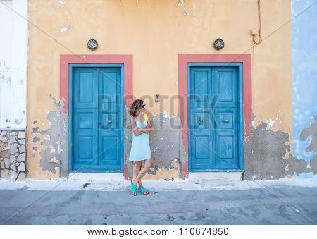 Yound blond woman at typical greek traditional town with colorful buildings on Kastelorizo Island, G