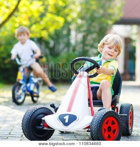 Little kid boy driving pedal car in summer garden