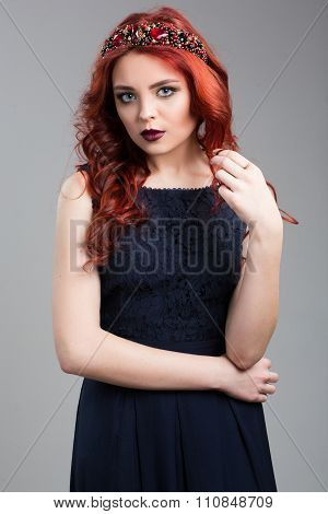 Beautiful red-haired fashion model posing in evening dress and in the diadem over dark background. f