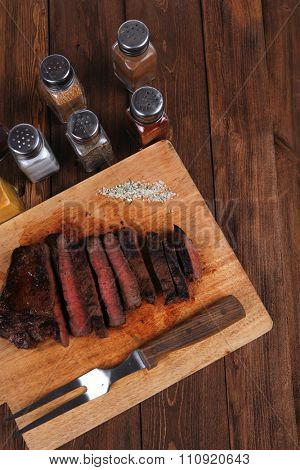 fresh roast red beef meat fillet mignon cutted on wooden plate with vintage fork many different kinds of dry spice over table