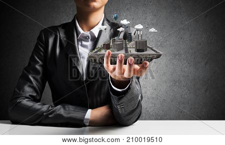 Cropped image of businessman in suit presenting in his hand modern city block with gray wall on background. 3D rendering.