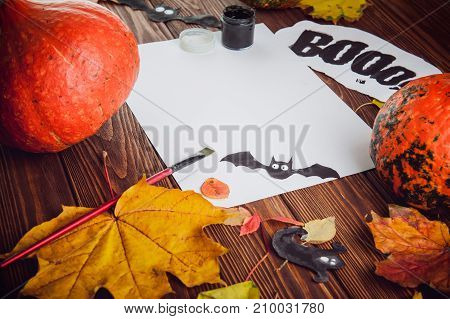 Halloween holiday background. Prepearing for party. Fresh pumpkins, coloured leaves, art, craft and painting materials on dark wooden table. Selective focus, top view. Space for text.