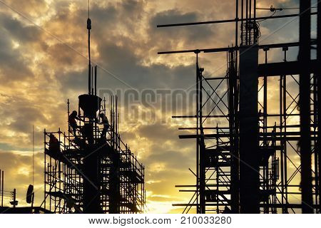 Silhouette civil site engineer and construction worker working on scaffolding in industrial construction during sunset sky background over time job