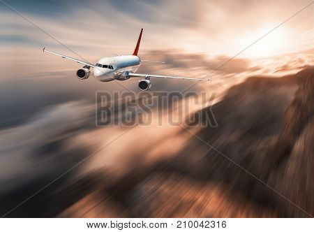 Modern airplane mith motion blur effect is flying over low clouds at sunset. Landscape with passenger airplane, blurred clouds, mountains, sun. Passenger aircraft. Commercial plane. Vintage style