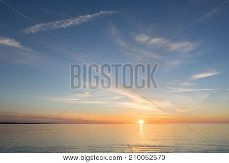 Evening sunlight on coast pink clouds blue sky reflection on water. Beach in summer. Seaside natural environment. Shore in Kesselaid small island in Estonia. Nature Reserve in North Europe
