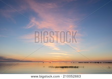 Evening sunlight on coast pink clouds blue sky reflection on water. Beach in summer. Seaside natural environment. Shore in Kesselaid small island in Estonia. Nature Reserve in North Europe