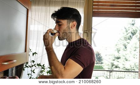 Young attractive man preparing a cup of espresso coffee with machine at home then drinking it