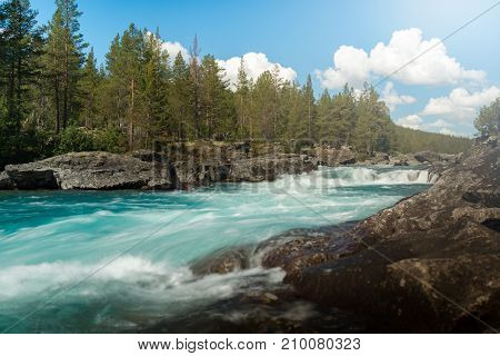 Fast river running through green forest in Norway Europe. Blue sky with clouds in background.