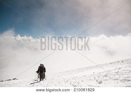 A group of mountaineers rises to the top of a snow-capped caucasian mountain against the backdrop of the rocky peaks of the mountains covered with snow.