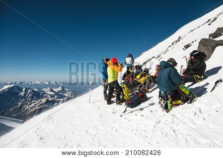 fully equipped Professional mountaineers on a stop sit on a snowy slope in sunny weather. The concept of collective recreation in the mountains