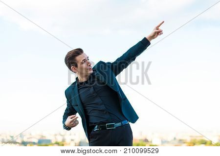 Young Serious Busunessman In Dark Suit, Watch And Black Shirt Stand On The Roof