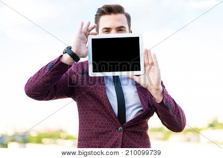 Serious Businessman In Red Suit And Shirt With Tie Stand On The Roof With Empty Tablet