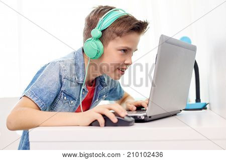 technology, gaming and people concept - boy in headphones playing video game on laptop computer at home