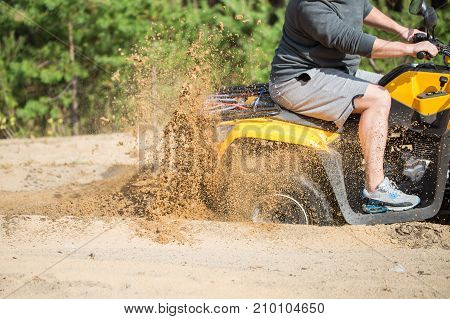 An Atv Quadbike Get Stuck In A Sandy Road Near Forest And Having Wheel-spin Making A Spray Of Sand