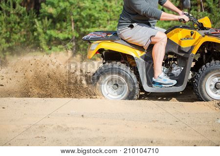 An Atv Quadbike Get Stuck In A Sandy Road Near Forest And Having Wheel-spin Making A Spray Of Sand