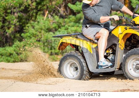 An Atv Quadbike Get Stuck In A Sandy Road Near Forest And Having Wheel-spin Making A Spray Of Sand