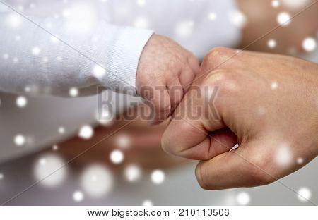 family, motherhood, people and child care concept - close up of mother and newborn baby hands making fist bump gesture over snow