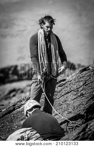 Black and white shot of two climber men with rope standing and sitting on mountain