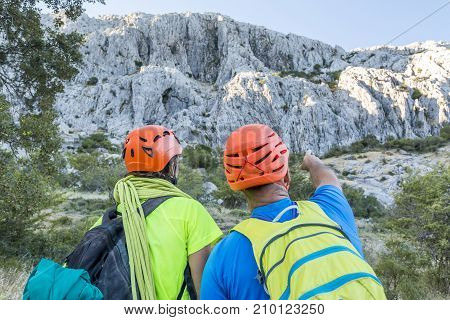 Two men in equipment for mountaineering standing at rock and looking away