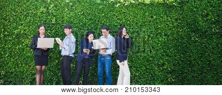 Businesswoman and businessman working outside office using laptop computer mobile phone and tablet device at green leaf wallmobile office conceptcopy space for adding text or designbanner size.