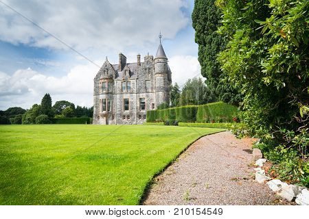 Pathway leading along side of large green lawn and tall trees to beautiful old castle