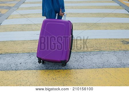 The girl drags a suitcase on wheels in the city on the crosswalk