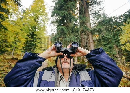 adult male forester in a jacket with a mustache examines the forest through binoculars. Hands and binoculars close-up.