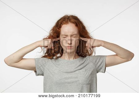 Stressed Frustrated Young Redhead Female Plugging Her Ears With Fingers And Keeping Eyes Closed Whil