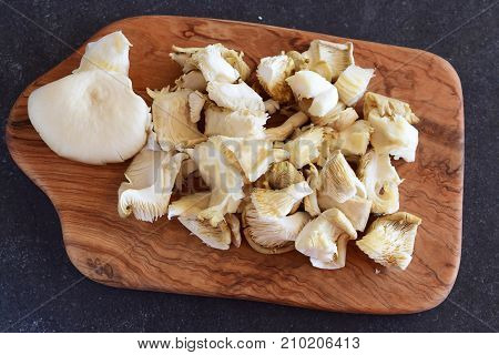 Fresh oyster mushrooms cut in big pieces on an olive wood cutting board on a grey abstract background. Step by step cooking
