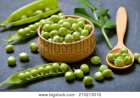 Green peas in bowl pods of peas on wooden table
