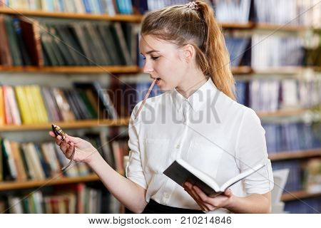 Pretty smiling student wathing on wristwatch. Beautiful girl posing on the camera and holding book in hand. Close-up of girl. Education concept.