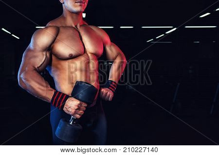 closeup of bodybuilder torso with dumbbell in hand. Bodybuilding concept. Copy space. Muscular man with sport bandages tapes on wrists. Power fitness man doing exercises with dumbbell in gym
