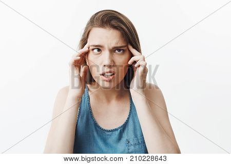 Portrait of funny beautiful young brunette woman with straight hair massaging head with finger, nowning eyes, having super tired look after receiving lot of tasks on work