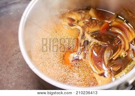 Flavor shank of lamb boiling in saucepan. Slow cooked leg of lamb with broth in casserole close up. Delicious food of european restaurant.