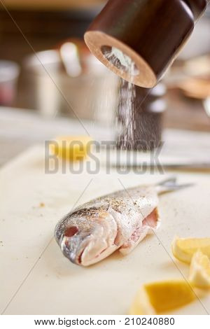Processing with salt raw fish. Process of cooking dorado fish with spices, salt and lemon. European restaurant kitchen.