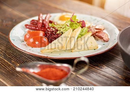 English breakfast on plate. English breakfast with toasts, tomatoes, beans, fried eggs, baked sausages and bakon. English breakfast in restaurant.