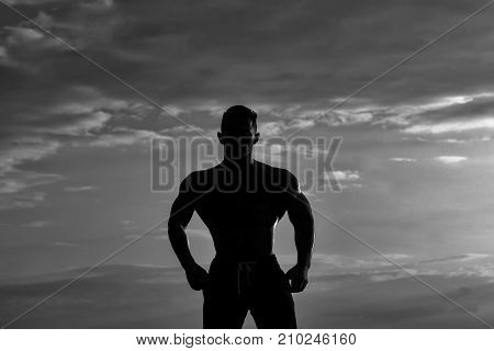 young macho man model athlete silhouette with muscular sexy body and bare chest outdoor on sky background