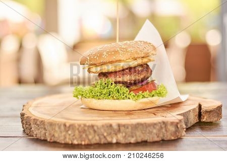 Appetizing cheeseburger on wood. Big humburger with cutlets, cheese, tomatoes, lettuce, onion, pickled cucumbers. Classic american food.