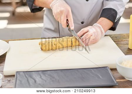 Male hands cutting long sushi roll. Japanese chef cutting sushi roll on white cutting board.