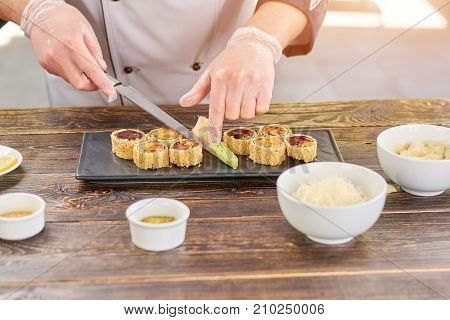 Chef serving sushi set with wasabi. Cook adding wasabi to sushi set on plate. Sushi preparation at kitchen.