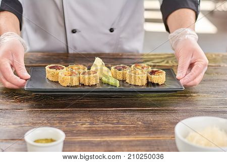 Chef hands holding plate with sushi rolls. Unagi sushi rolls on traditional japanese dish in cook hands. Sushi with eel and avocado.