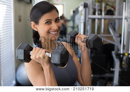 Closeup portrait young attractive woman lifting weight in gym indoors with equipment in the background